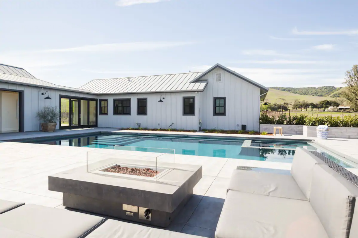 Outdoor seating around a minimalist firepit, with a rectangular pool + spa and house in the background.