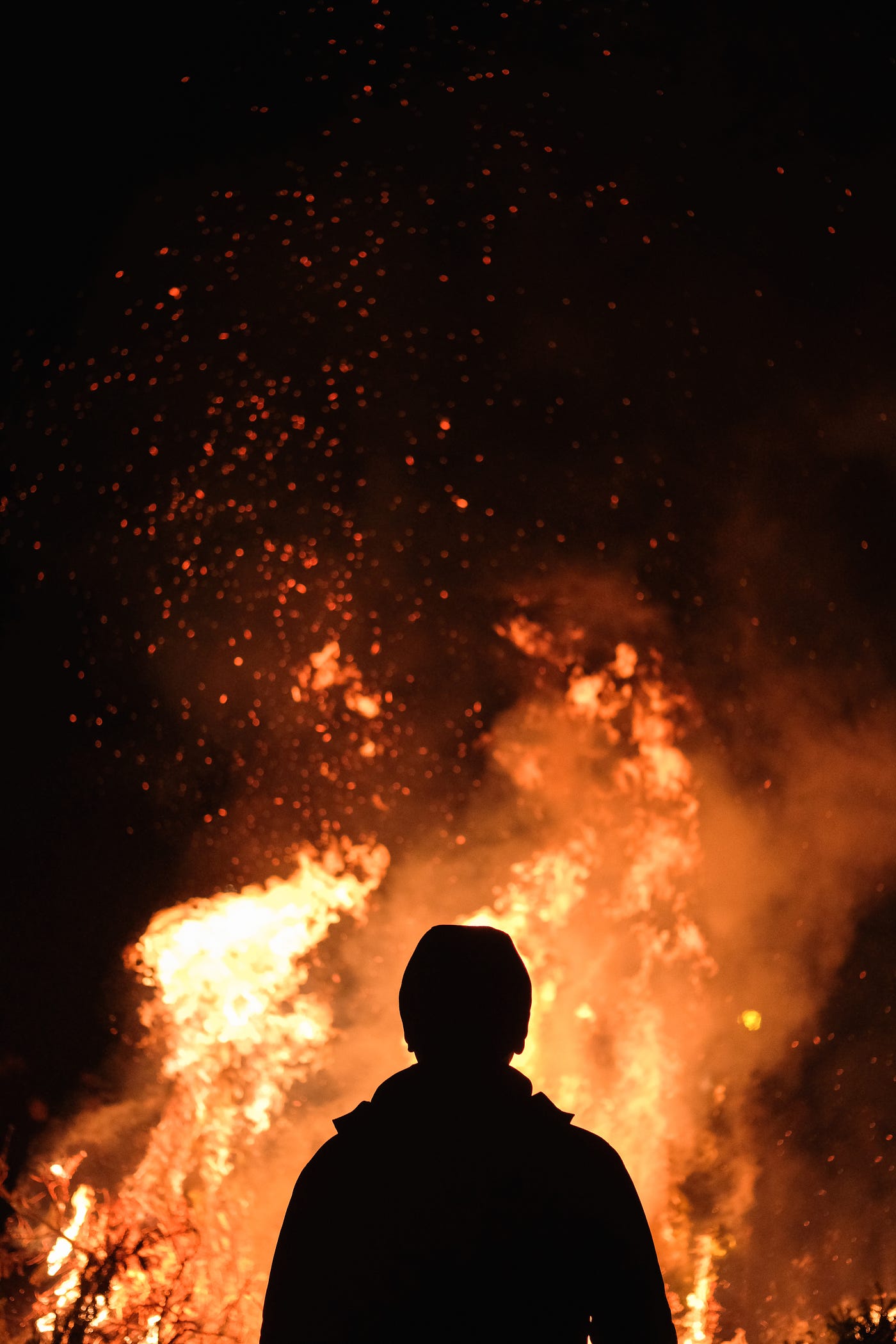 A silhouette of a person in front of tall flames and sparks.