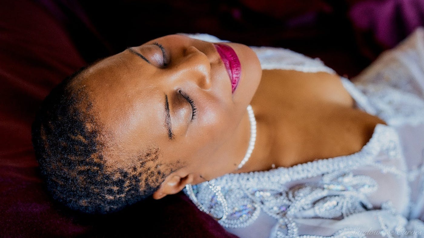 A Black woman with extremely close-cropped hair lying back, smiling and closing her eyes.