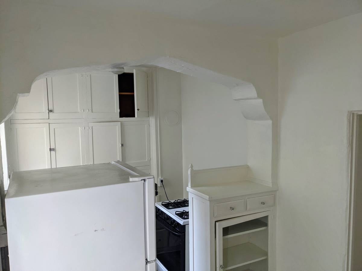 A fridge blocking off most of the view of a kitchen. The stove’s plugged into a wall outlet about two feet away from it.