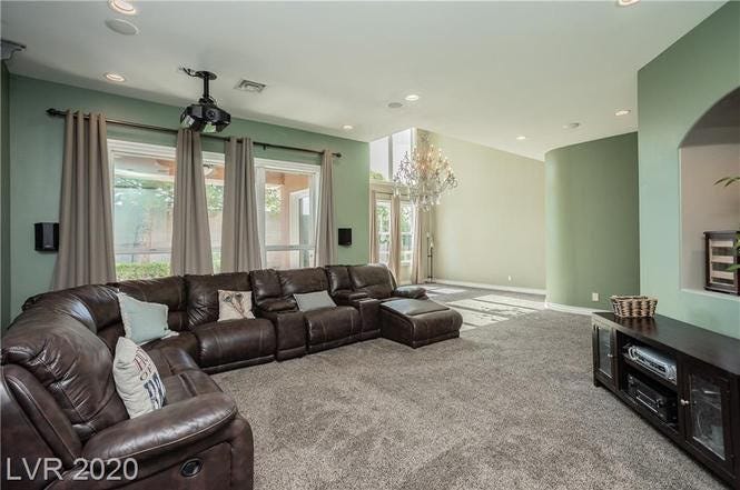 A carpeted living room with a large L-shaped leather couch. The walls are green.