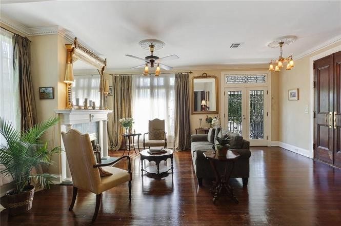 A large room with dark floors, tan walls, and ornate, formal furniture by a fireplace.