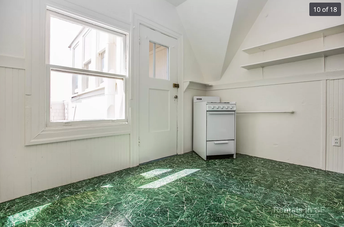 A white oven awkwardly placed in the corner of an otherwise empty room with green vinyl flooring.
