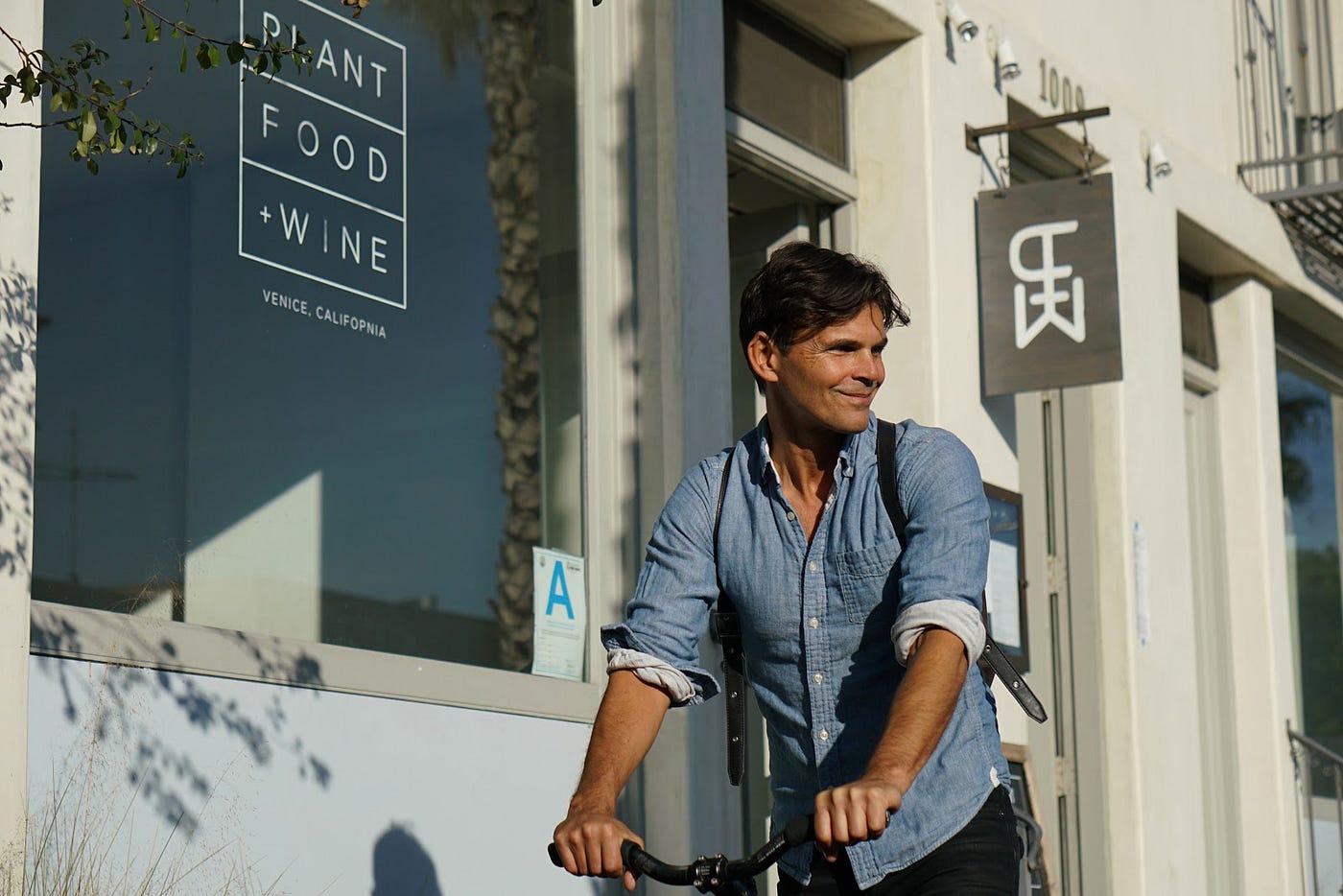 Chef Matthew Kenney riding a bike outside of Plant Food + Wine.