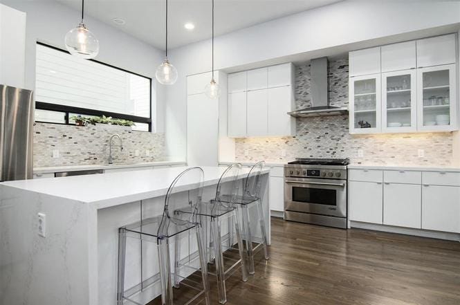 A white kitchen with a island with bar seating and a stainless steel stove and cabinets in the background.