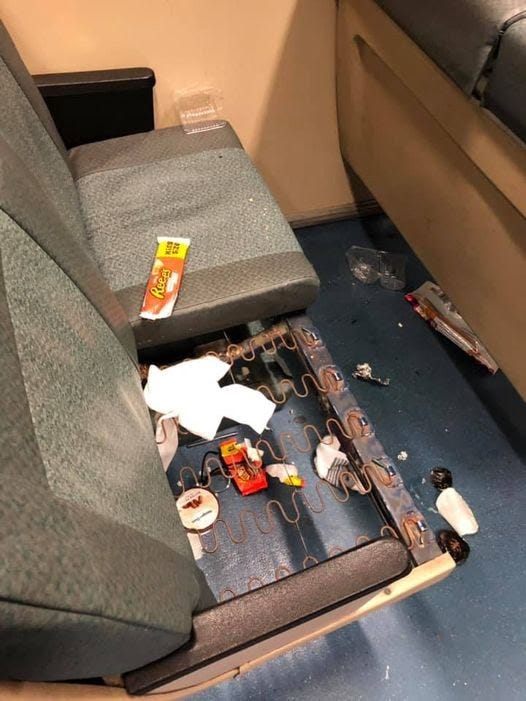 A row of 2 BART seats. One of them is missing a cushion and is covered in candy bar wrappers and other trash.