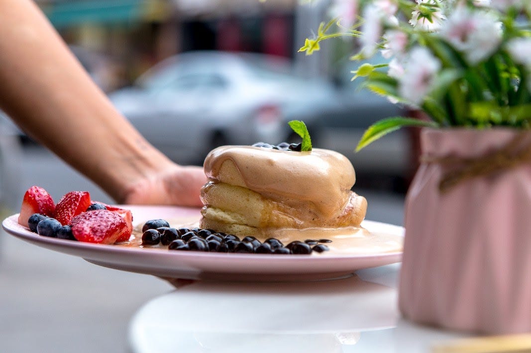 A plate with thick, fluffy pancakes covered in a tan sauce and surrounded by strawberries and blueberries.