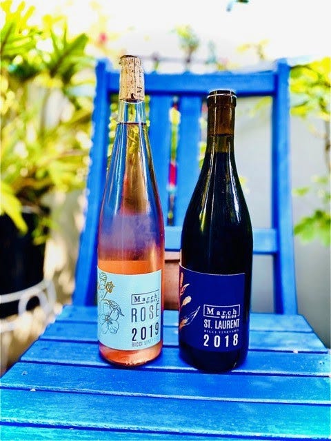 2 bottles of March Wines wine—2019 rosé and 2018 St. Laurent—on a blue wooden chair outside.