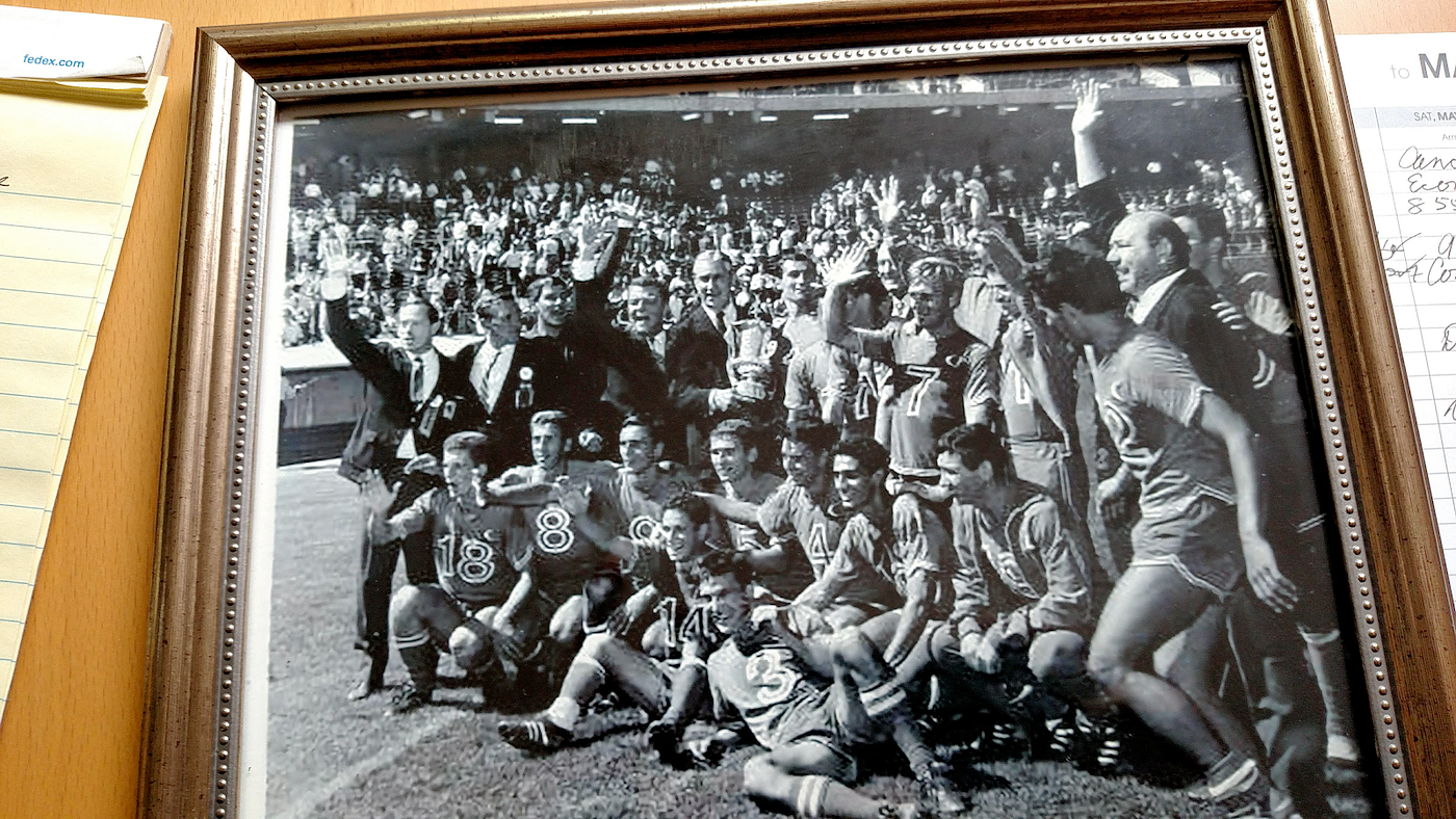 A framed black-and-white photo of a group of athletes posing and waving on a field.