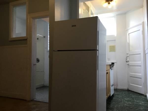 A tiny kitchen in the background, with the fridge in the foreground more or less in the hallway.