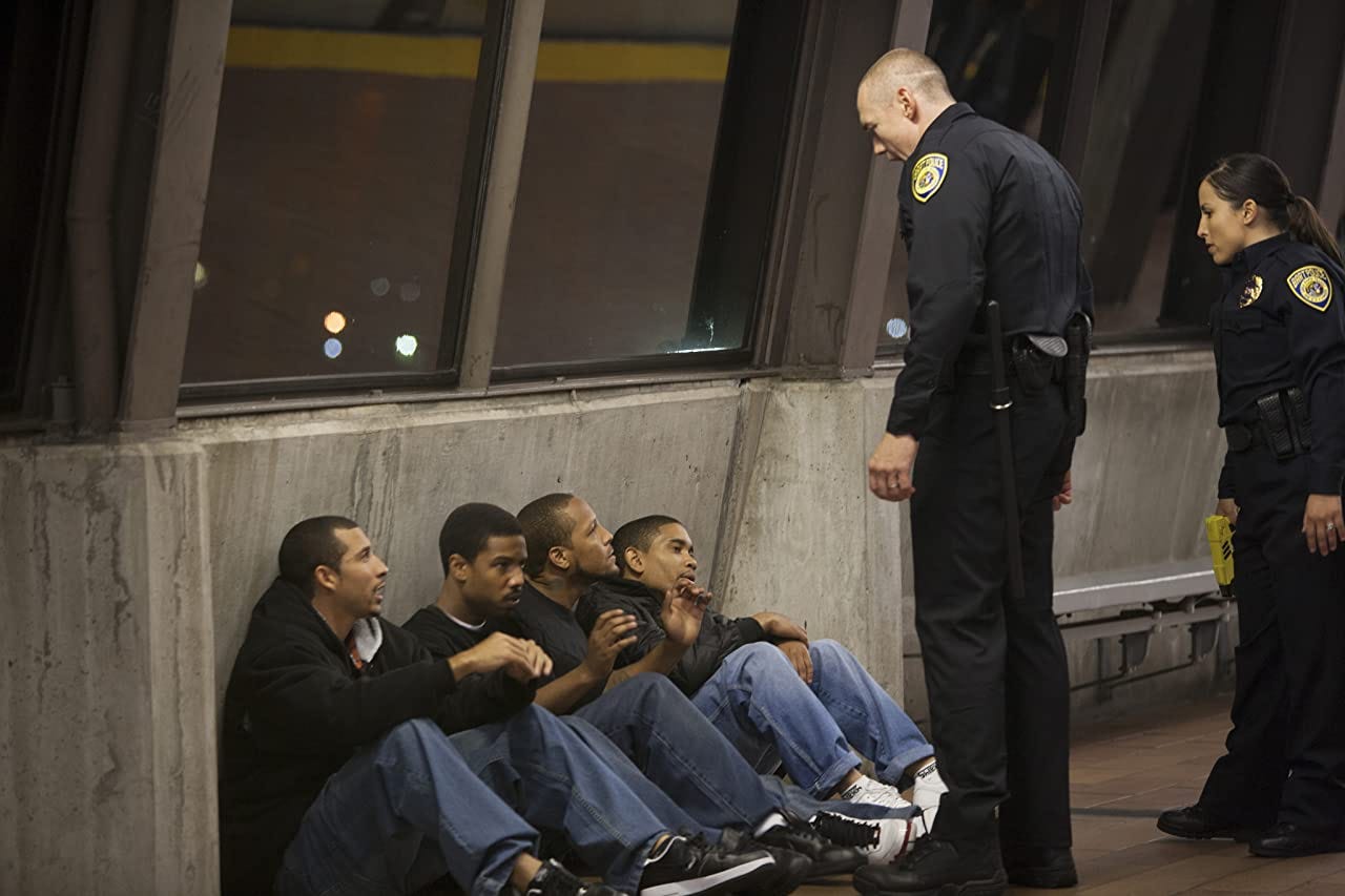 2 BART officers standing over 4 seated men on the Fruitvale BART platform.