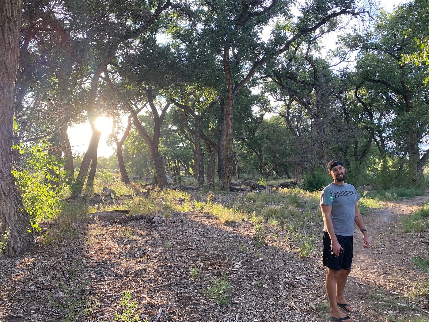 Cameron Price smiling in front of a small grove of trees, backlit by the late afternoon sun.
