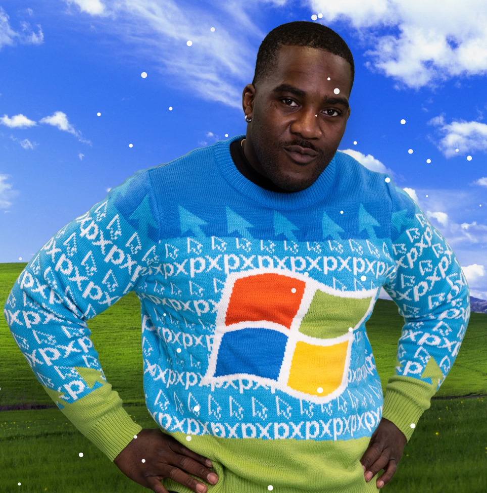 A person with shaved hair and dark skin wearing a Windows XP symbol on it, with the default XP hill desktop in the background