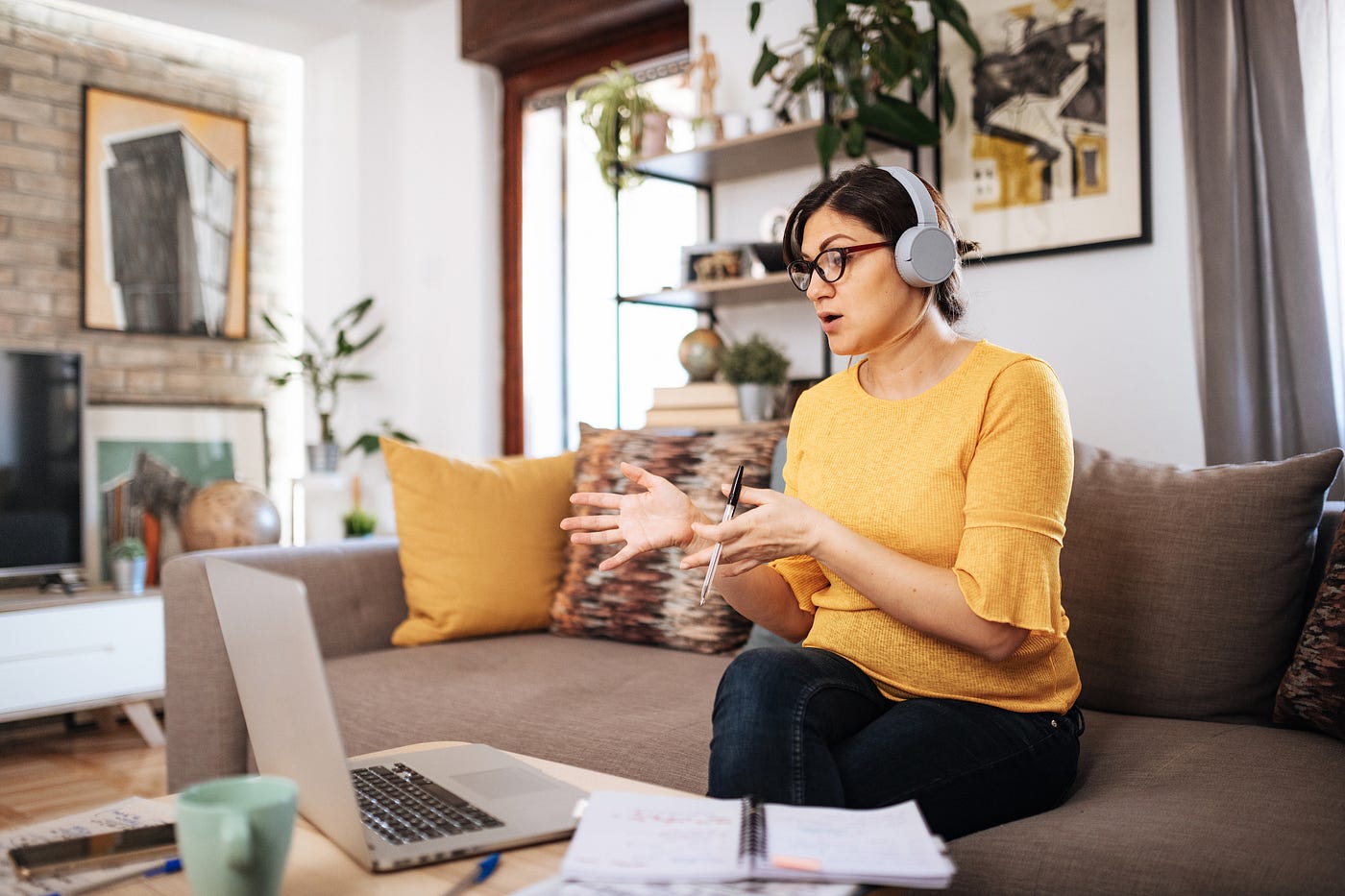 A person wearing headphones sitting on a couch speaking to someone on a video call on a laptop.