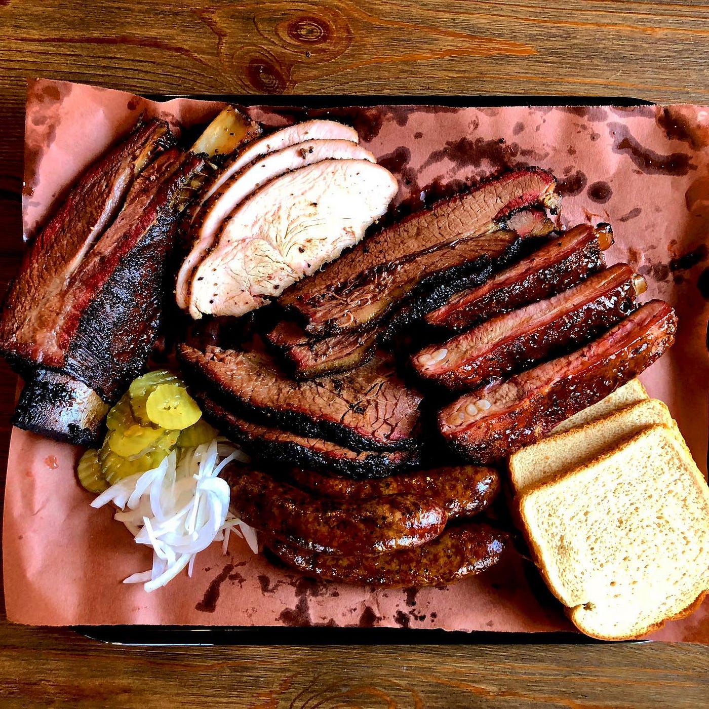 A square platter of sliced, barbecued meat and slices of bread.