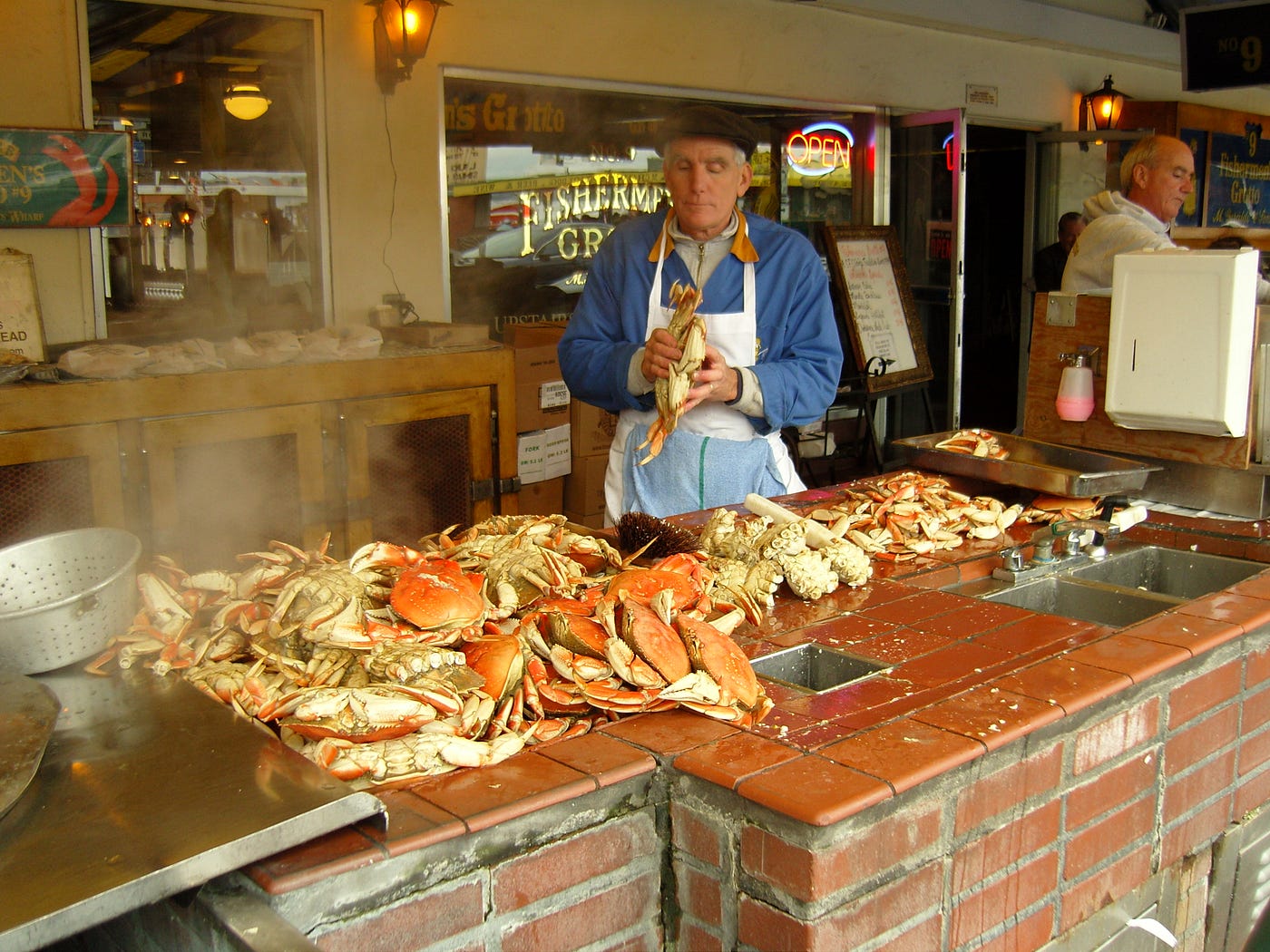 A person wearing an apron, preparing crabs at a workstation with a brown-tiled countertop.