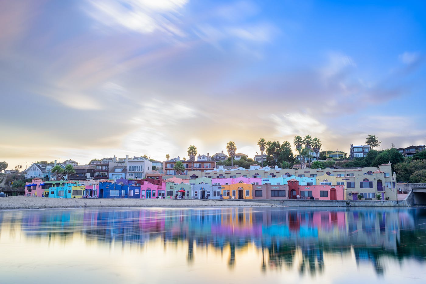A row of multicolored pastel houses right in front of a body of water before sunset.