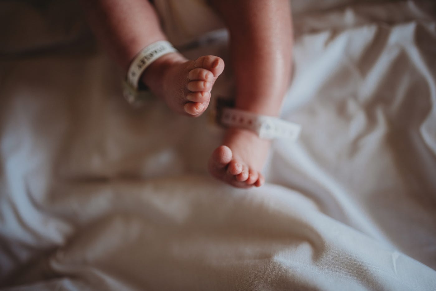Closeup of a light skinned newborn baby’s legs with hospital bracelets on the ankles.