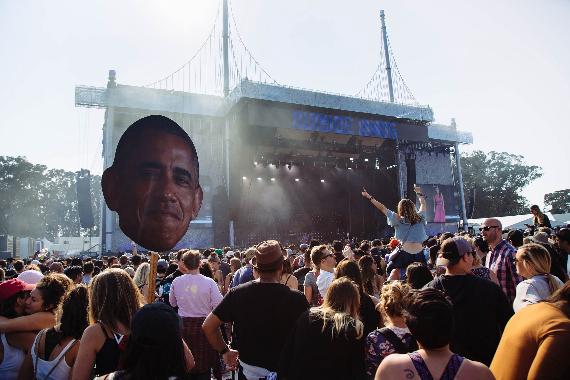 A photo of a crowd in front of a stage at Outside Lands. Someone is holding up a large cutout of Barack Obama’s head.