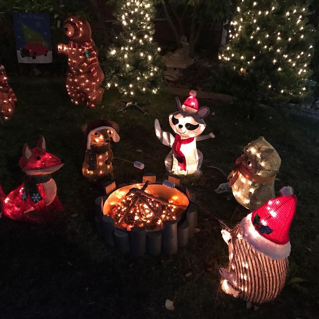 A group of inflatable animal Christmas decorations outside around a decorative fire pit, illuminated by Christmas lights.