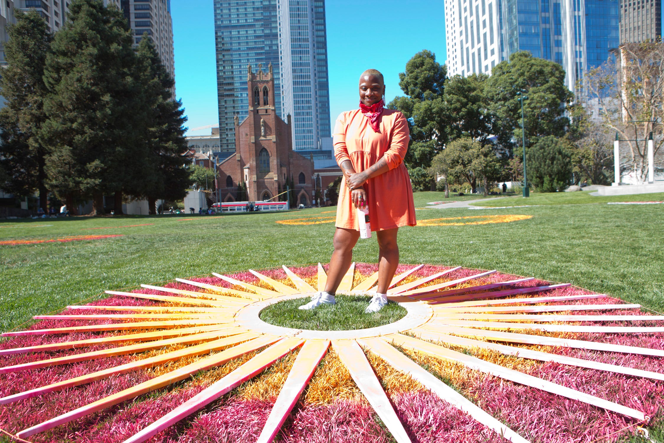 A person stands in the center of a large red/yellow gradient circle with radiating white lines painted on the grass