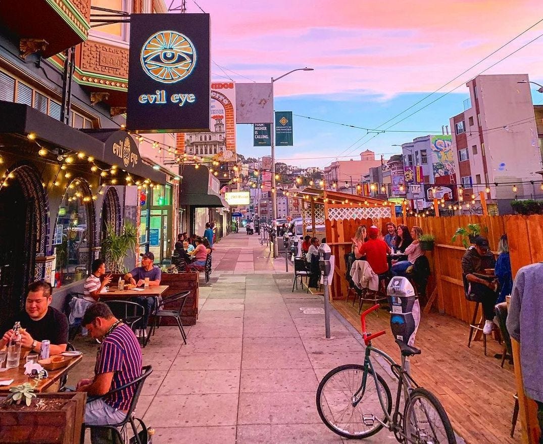 Evil Eye’s sidewalk dining space. Tables against the building and a fenced area near the street.