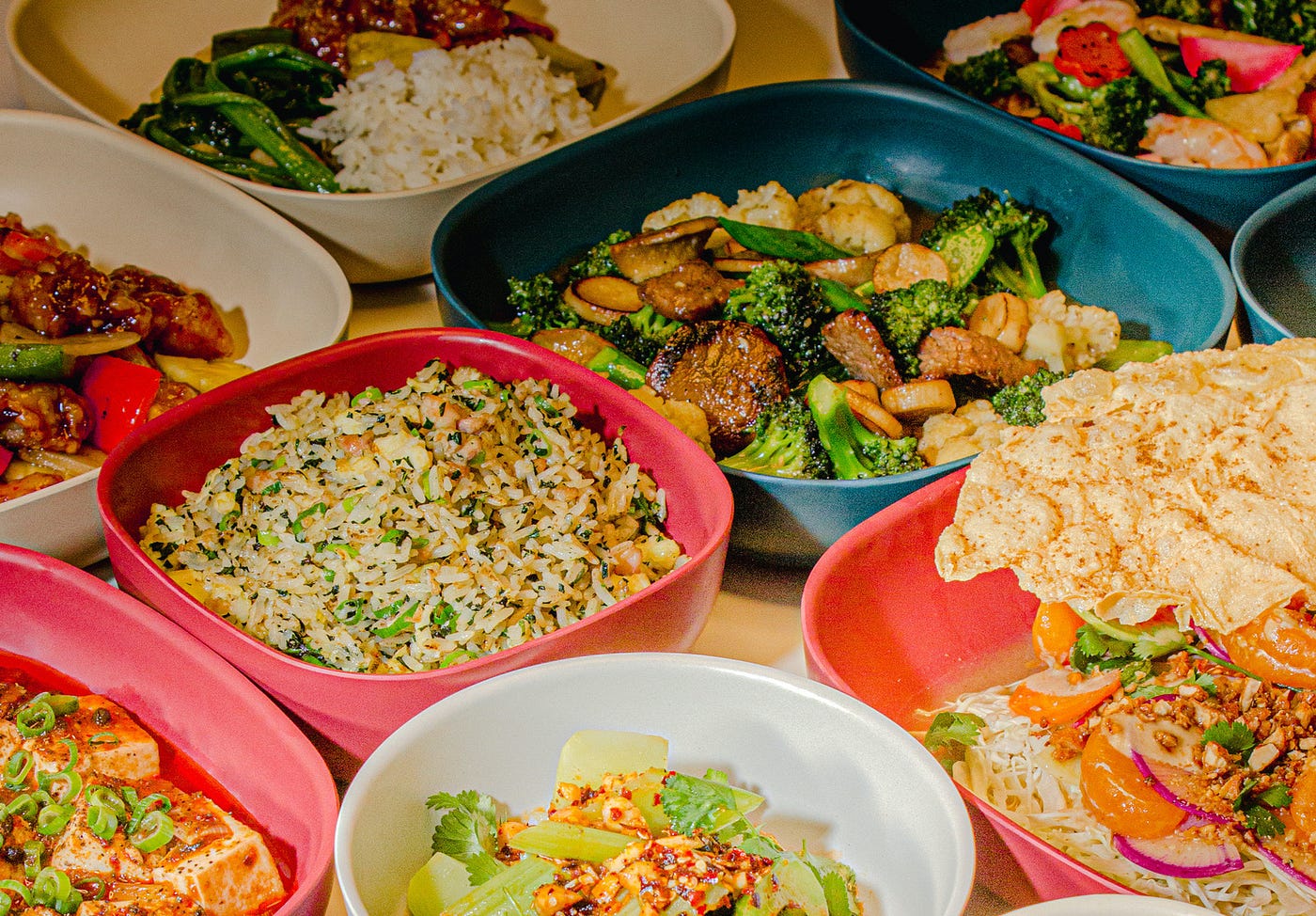 A variety of Chinese dishes served in multicolored bowls that are squarish with rounded corners.