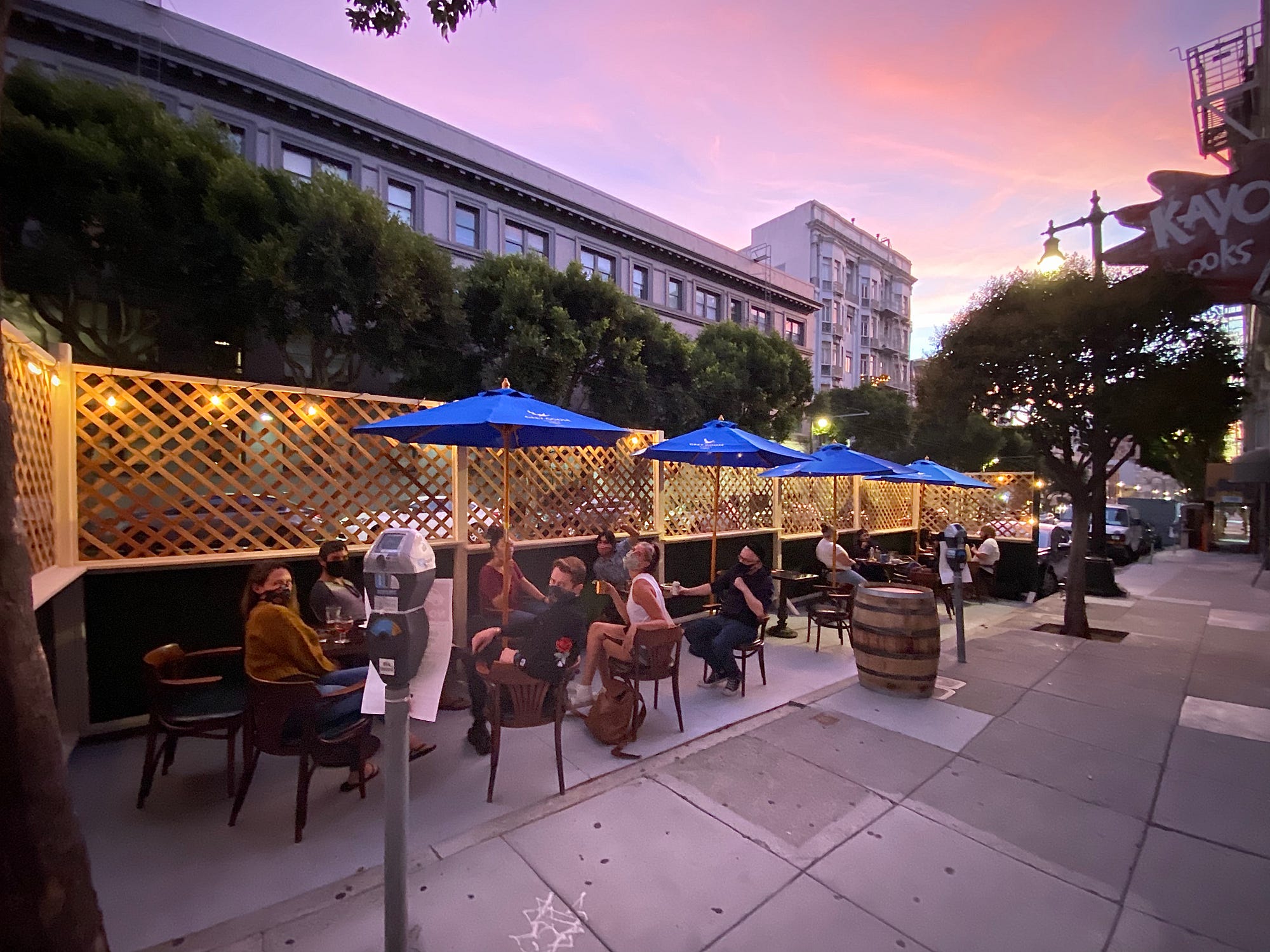 An outdoor dining space with four tables, defined by wooden lattice panels strung with lights.