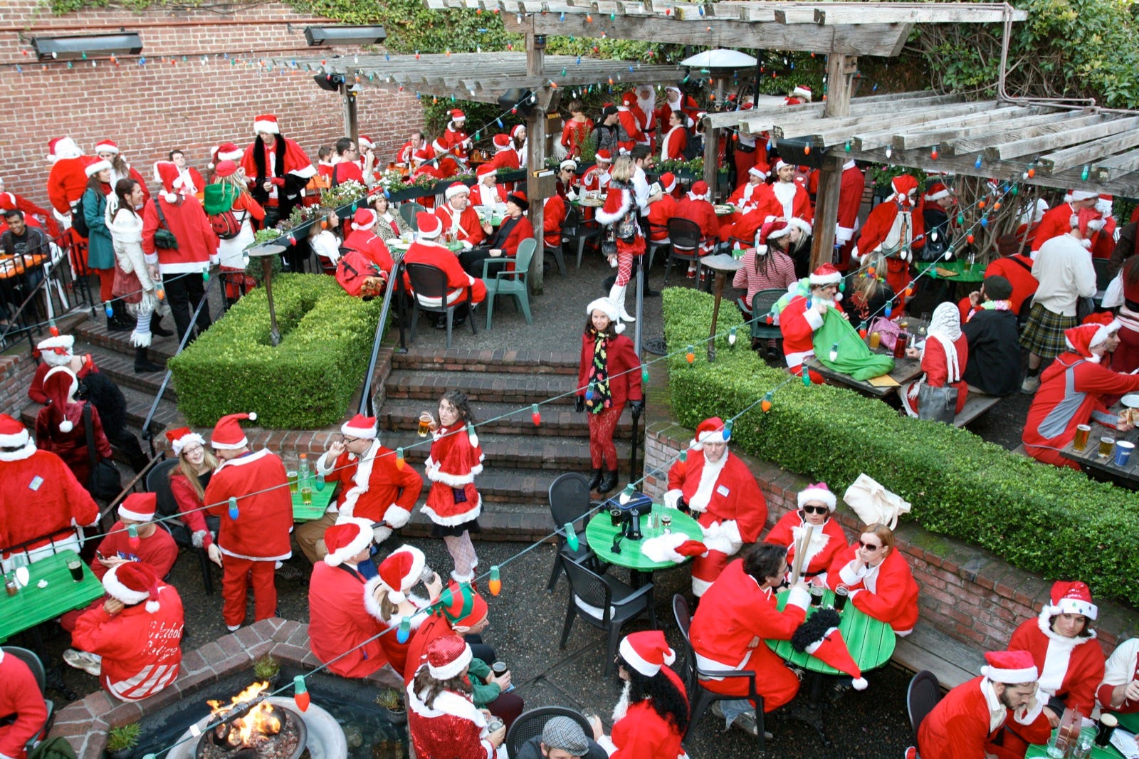 Dozens of people dressed as Santa sitting on the back patio of an eating establishment.