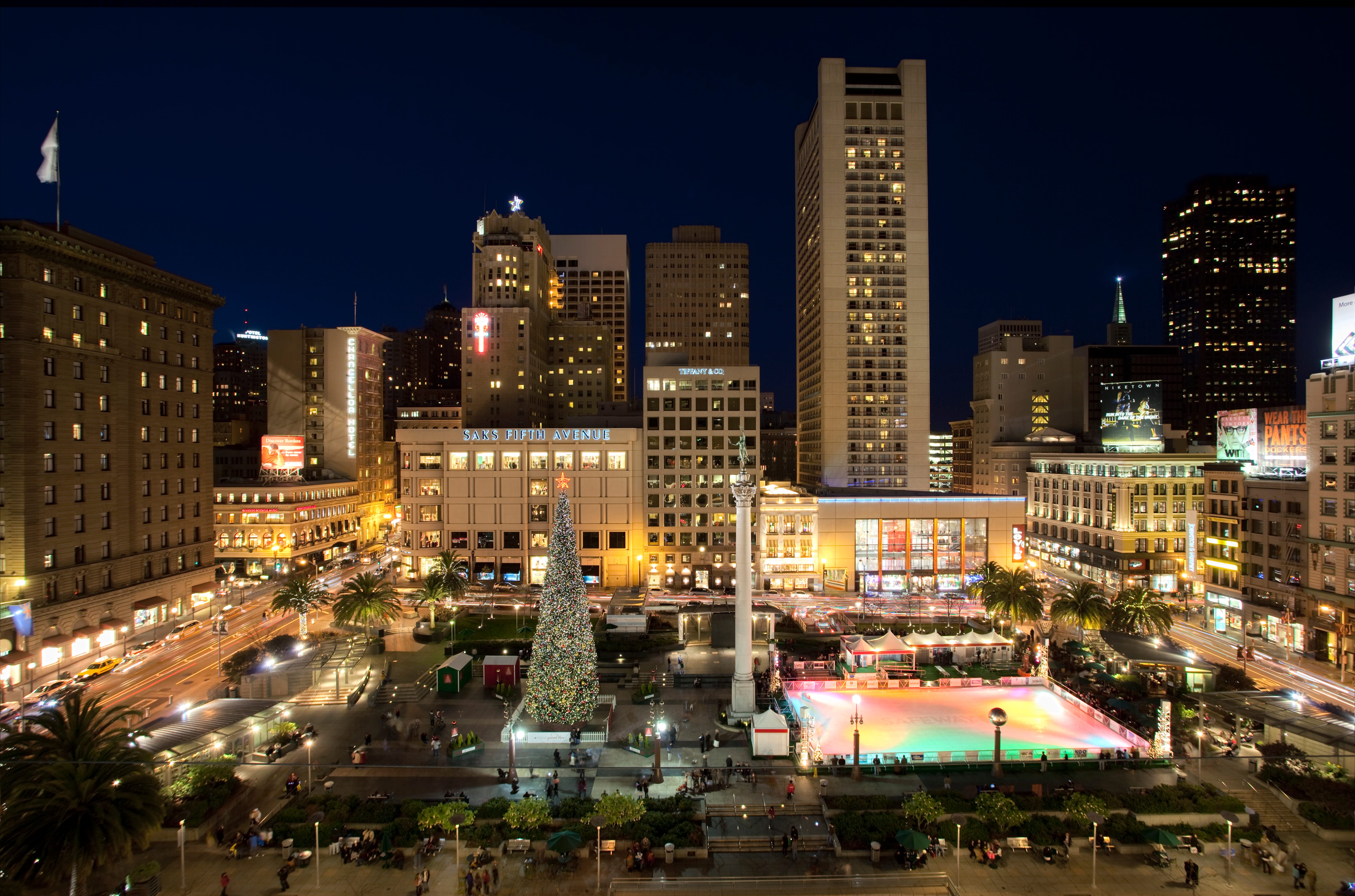 Union Square with a tall holiday tree and an ice skating rink, lit up at night.