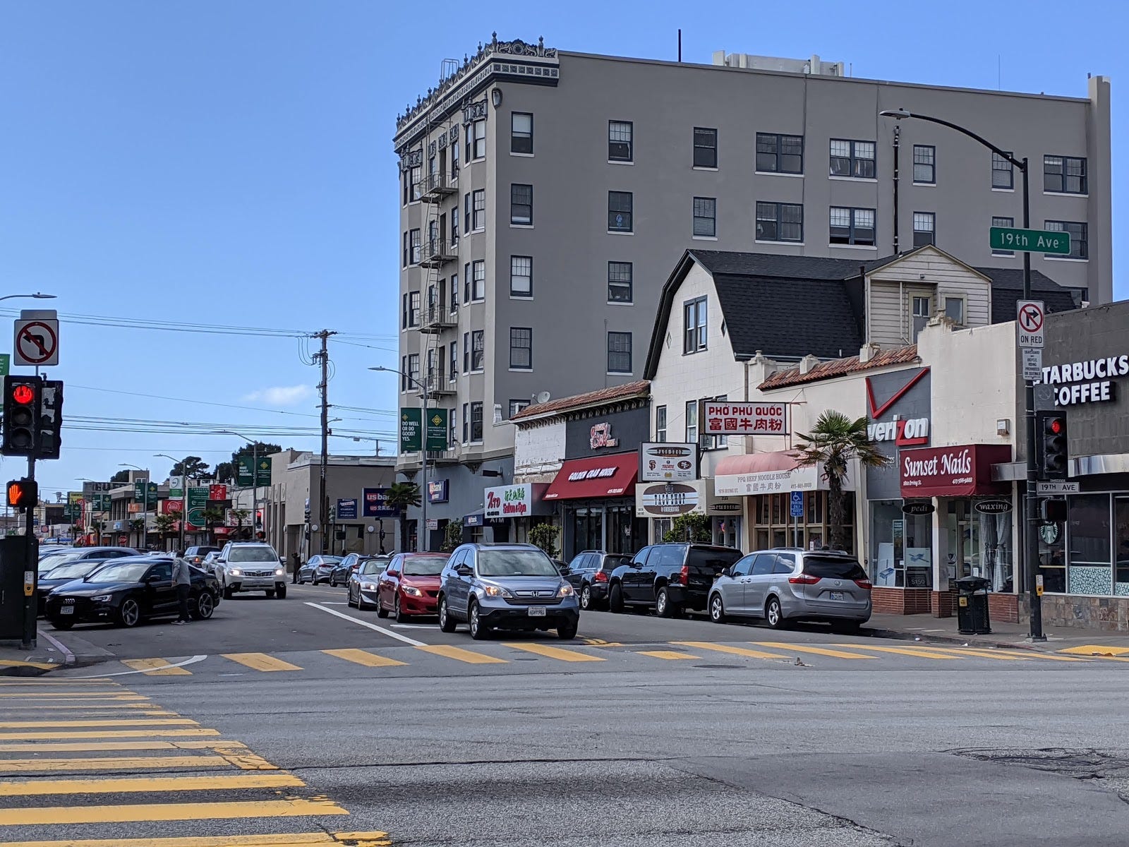 A view of a street with a large apartment building and a row of shops and restaurants.