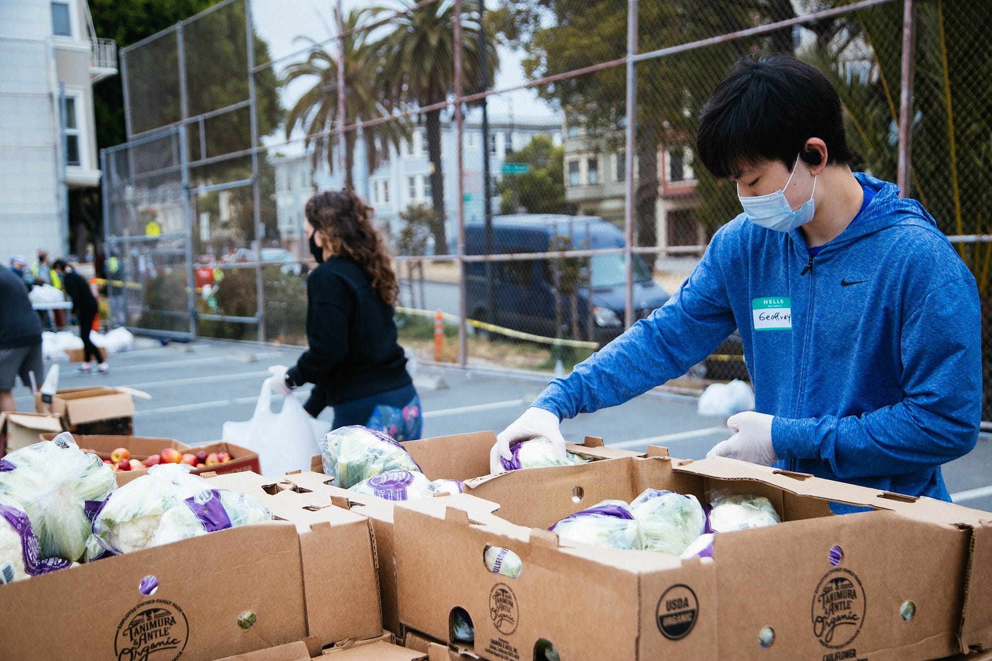 People taking food from cardboard boxes in a parking lot in a residential area.