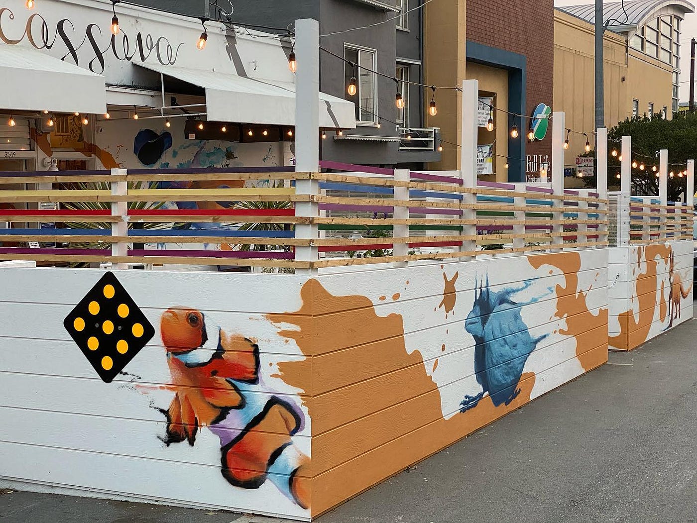 A fenced-in outdoor dining area at Cassava. The fence is painted with orange splotches and tropical fish.