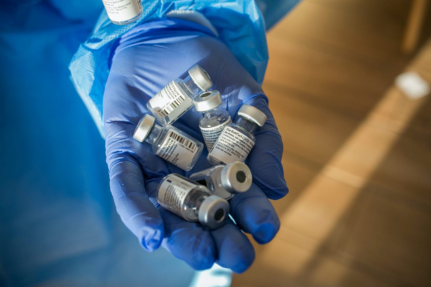 A person’s hand with a medical exam glove on, holding five vials of Covid vaccine in their palm.