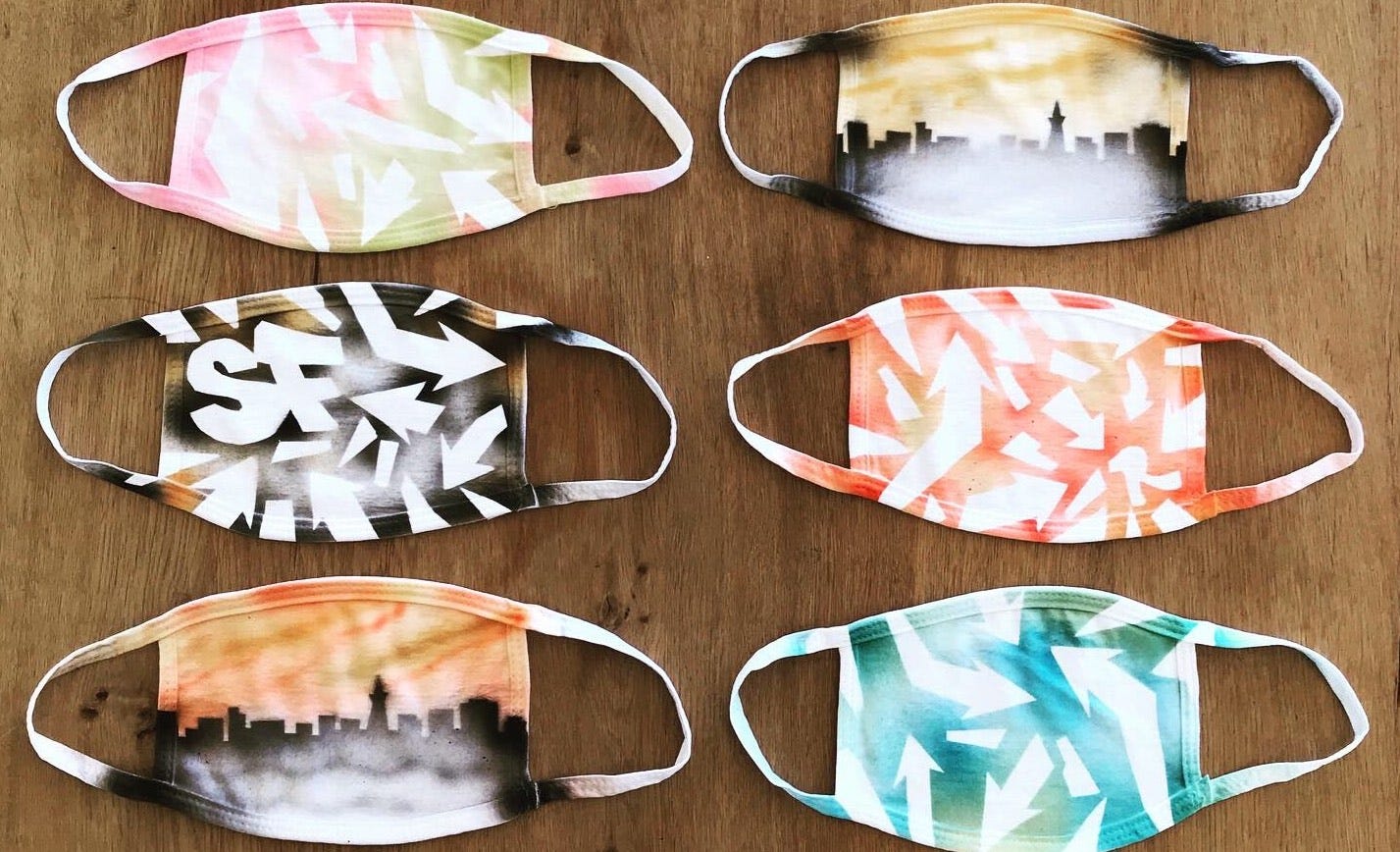 6 face masks, airbrushed with skylines and abstract designs, neatly arranged on a wooden surface.