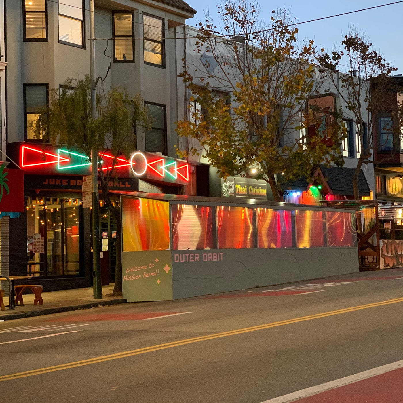 A street dining area in front of Outer Orbit, seen at dusk.