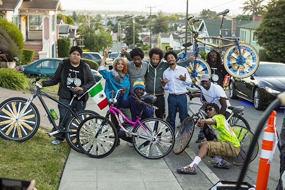 Characters from the movie posing with tricked-out bikes on a hilly Oakland street.