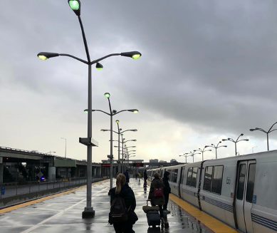 An open-air BART platform with a few passengers walking on a gray day.