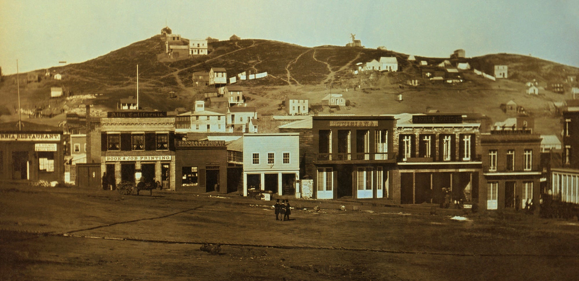 Sepia-toned photo of a row of buildings in San Francisco, hills in the background and open grass in the foreground.