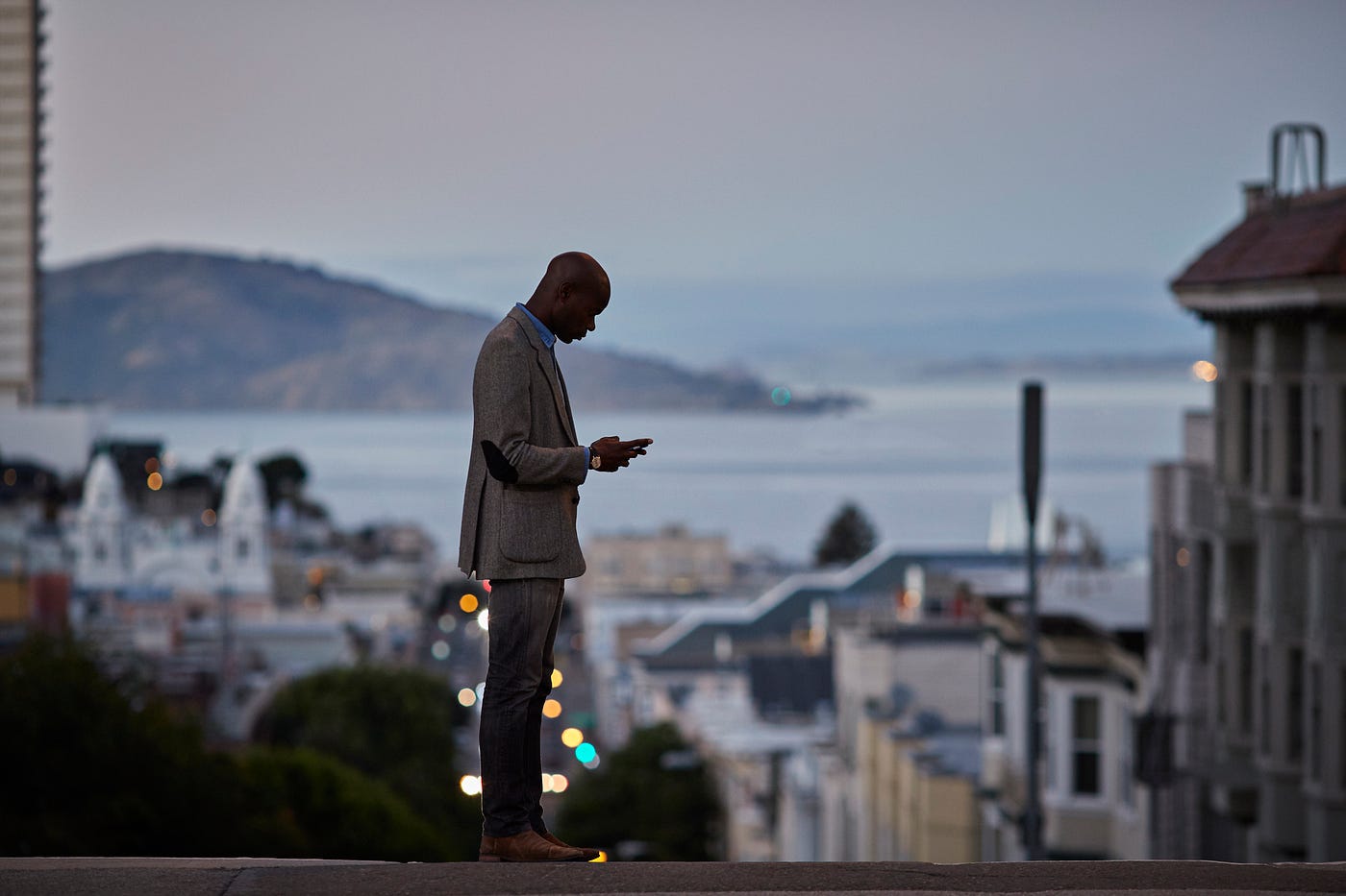 Black businessman checking phone while on the street in San Francisco in the evening.