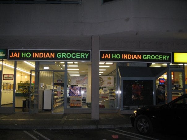 The Jai Ho Indian Grocery storefront: Floor-to-ceiling windows show a small, neat store with shelves.